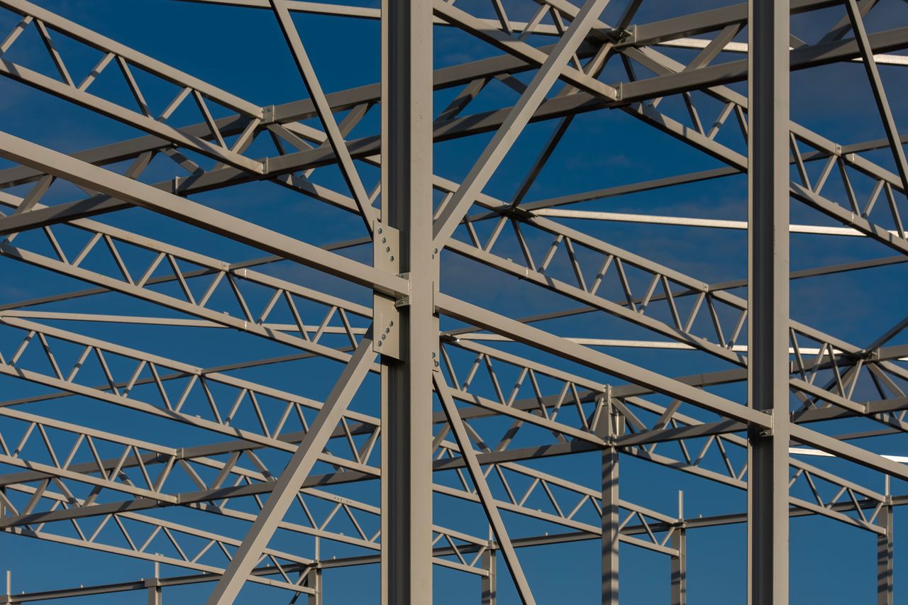 who-we-are Detailed view of a steel framework structure against a blue sky, showcasing modern construction elements.